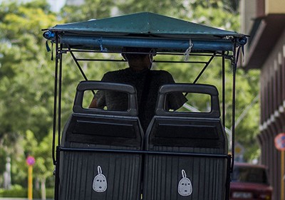 Foto: Julio César Guanche hombre conduciendo una bicicleta con toldo verde y dos asientos atrás con el capitolio cubano en frente
