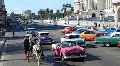 Autos antiguos de muchos colores comparten la carretera con una calesa