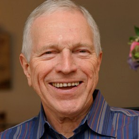 Man with grey hair and dark shirt smiling looking at the camera