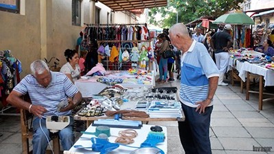 hombre sentado detrás de mesa con bienes a la venta reparando teléfono para hombre parado en frente en un mercado al aire libre