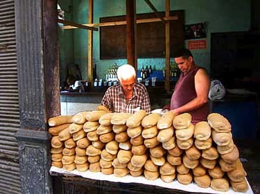two men in front of a counter piled with loaves of bread with a green background wall