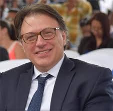 Julio Carranza Hombre con traje azul y camisa blanca con anteojos mirando a la cámara y sonriendo