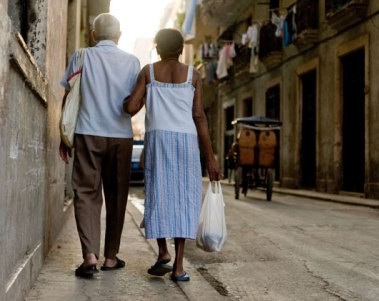 Photo: Trabajadores.cu elderly man wearing a white shirt and woman wearing a blue skirt walking arm-in-arm down a narrow street