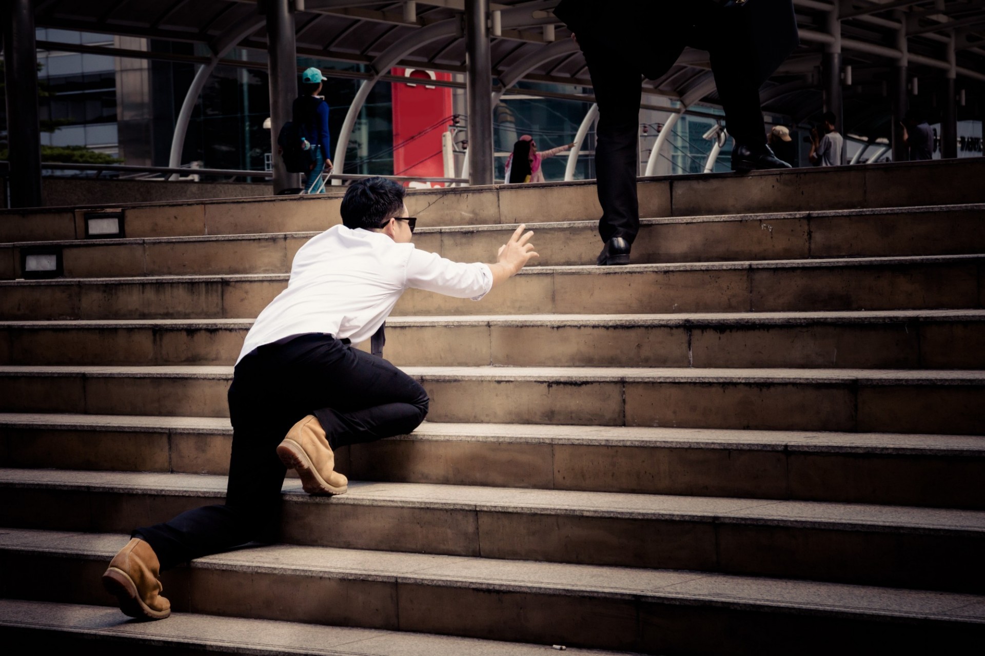 man dressed with white shirt crawling up a staircase and trying to catch up with others