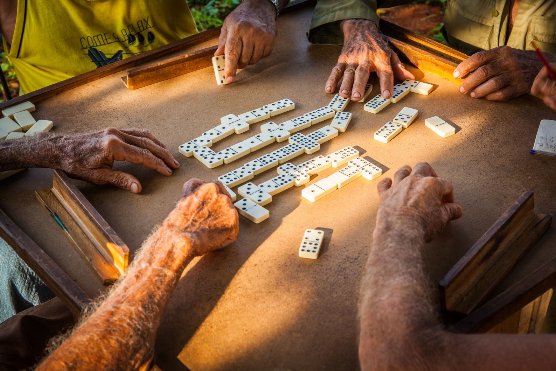 Manos de ancianos jugando al dominó en una mesa cuadrada.
