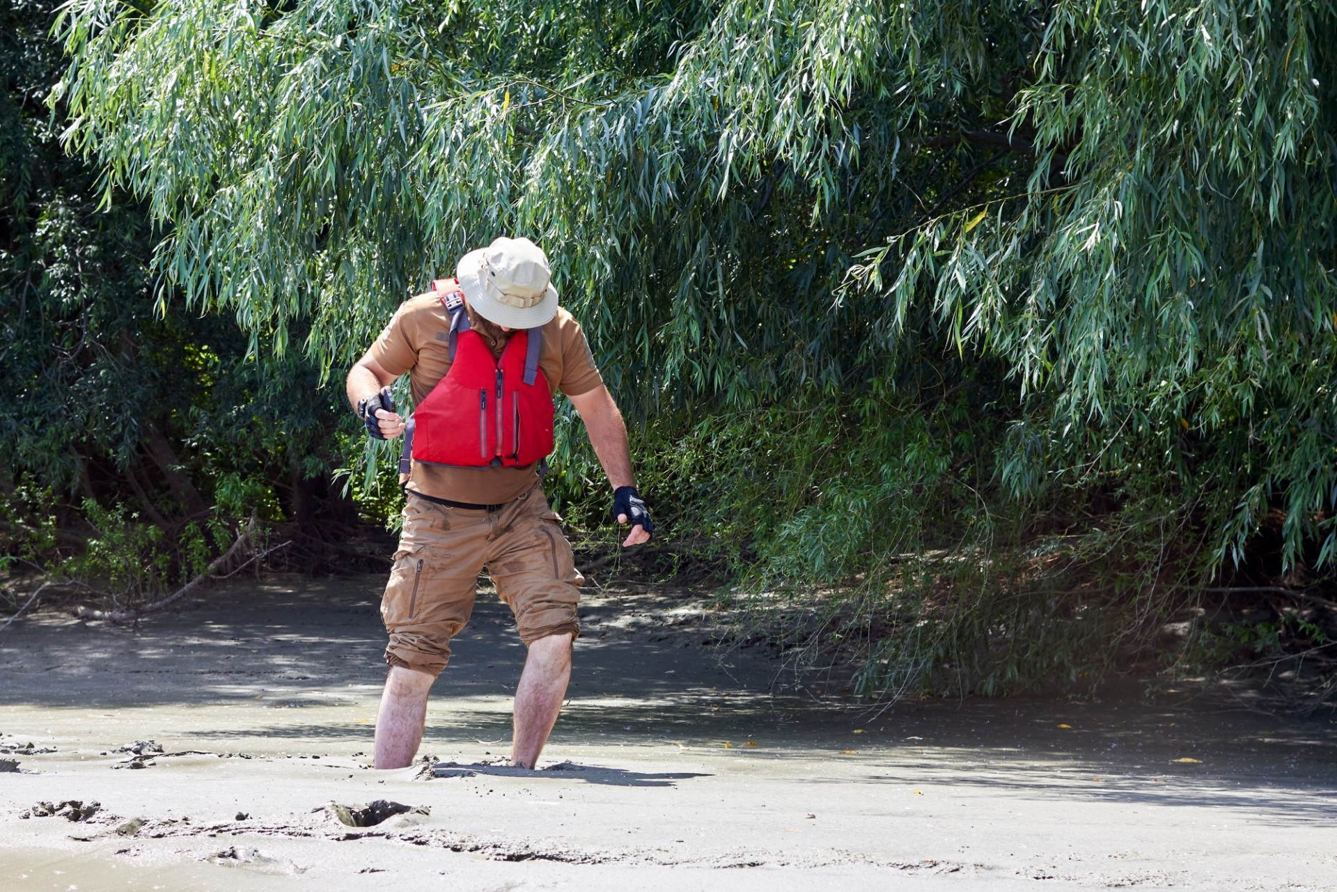 hombre con chaleco rojo y sombrero blanco tratando de liberarse del pantano
