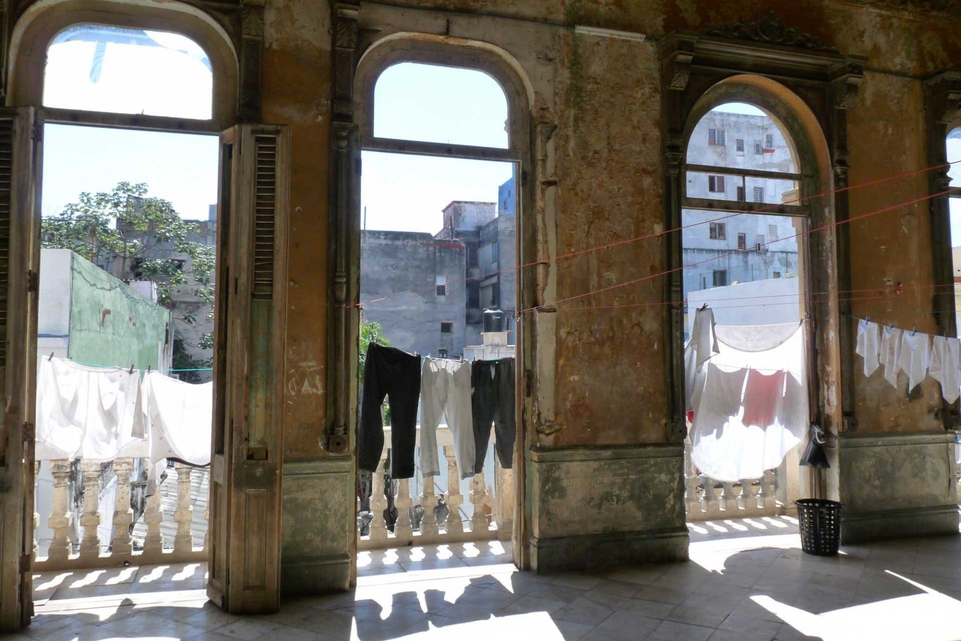 interior deteriorado con grandes ventanales hacia a terraza llena de ropa lavada colgada 