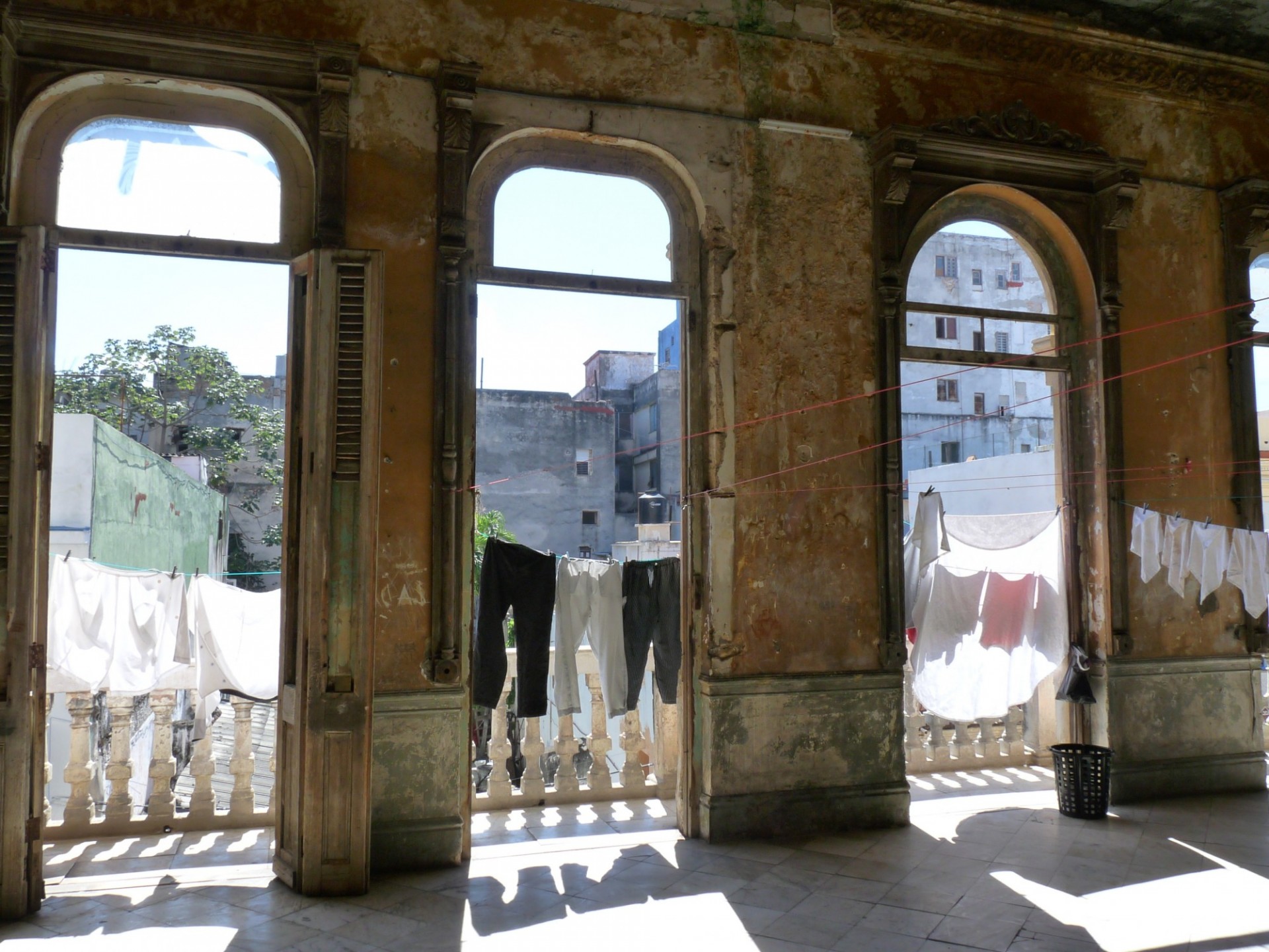 Deteriorating interior with large open windows looking out on a terrace full of clothing hung out to dry.