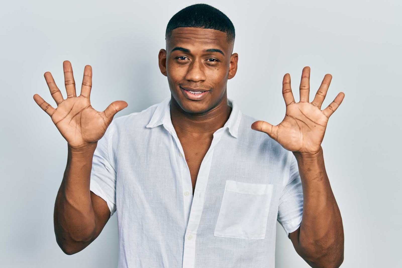 dark skinned man with white shirt holding up hands with 10 fingers