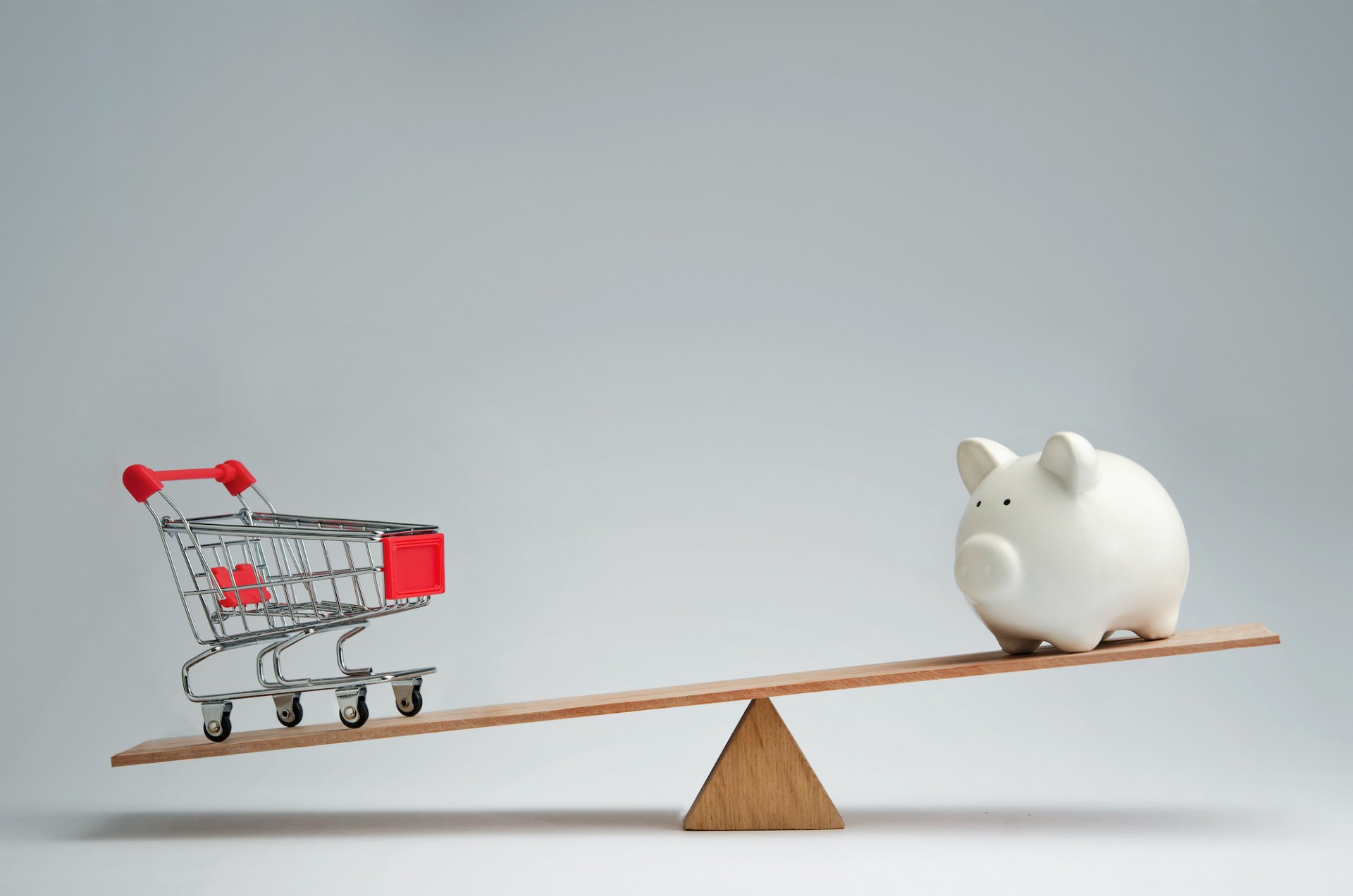 empty shopping cart balanced on a see saw with a piggy bank