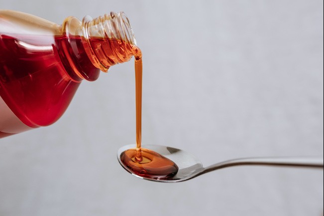 bottle of red medicine pouring out into a spoon
