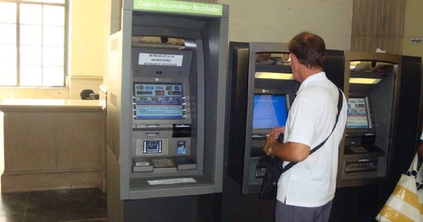 hombre con camisa blanca de espaldas mirando cajeros automáticos en un banco en Cuba