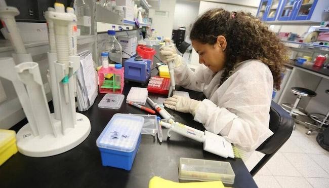 Mujer vestida de blanco en un mostrador de laboratorio con un implemento en la mano.