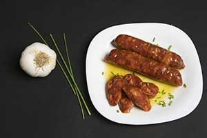 Dos chorizos en un plato blanco con un fondo negro y un ajo