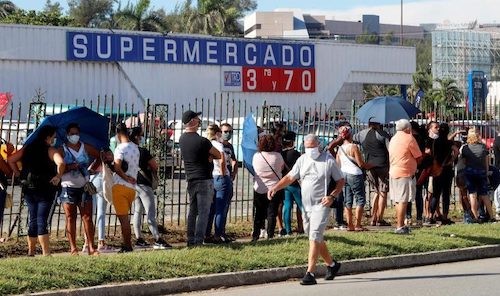 cola de personas a lo largo de una reja, algunas con parasoles, esperando entrar al Supermercado 3ra y 70 en La Habana