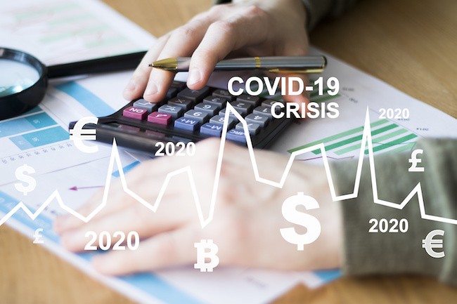 Image of two hands with a calculator and magnifying glass on top of papers with a graph in white with the signs of various world currencies