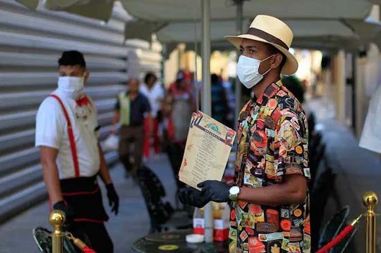 hombre de camisa multicolores y sombrero de paja esperando llegada de turistas aguantando documentos