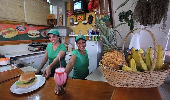 women dressed in green, smiling, serving a hamburger and a shake
