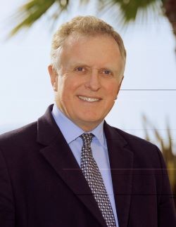 smiling man with dark blue suit and tie and light blue background