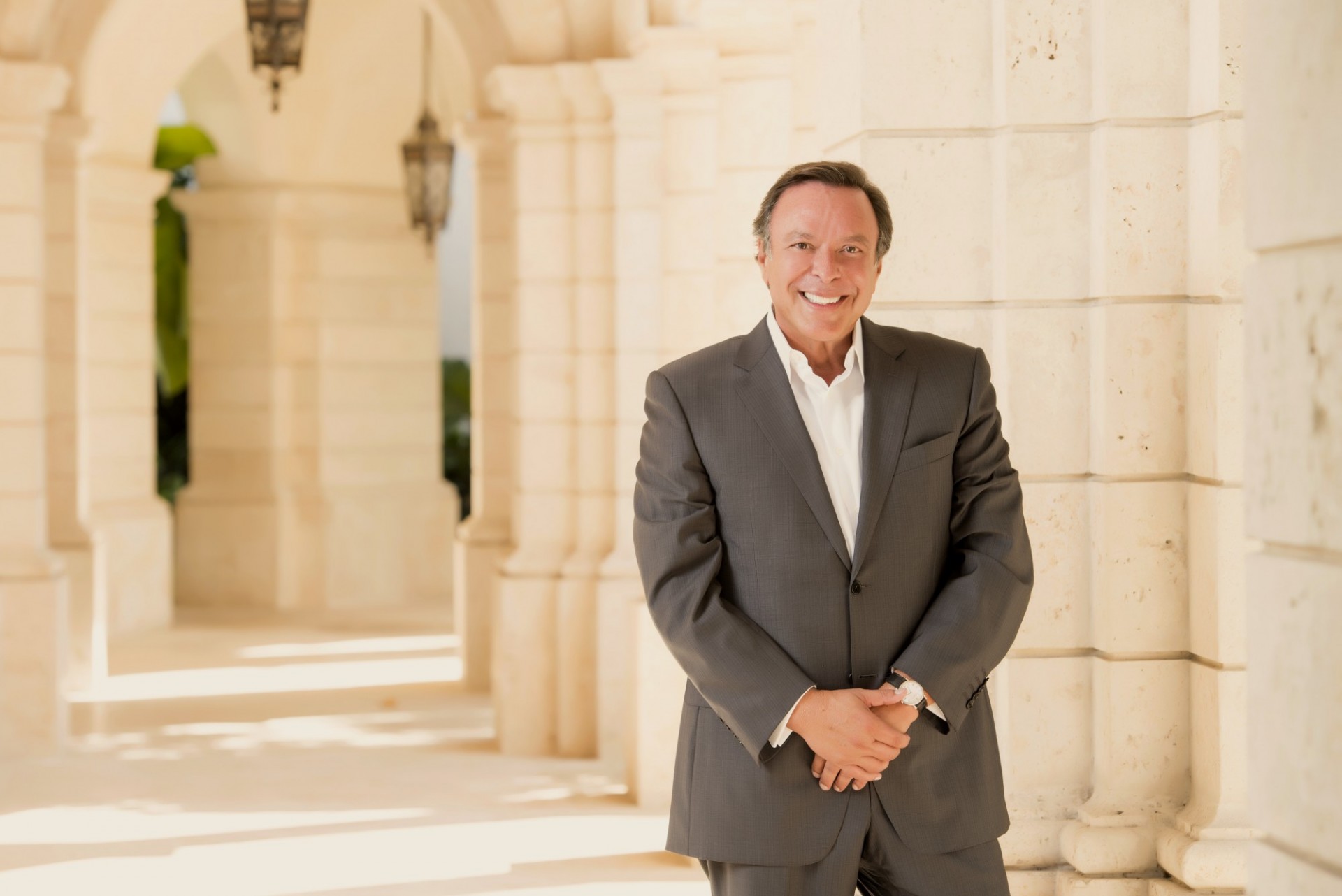 man in dark suit with white shirt standing in front of columned walk way