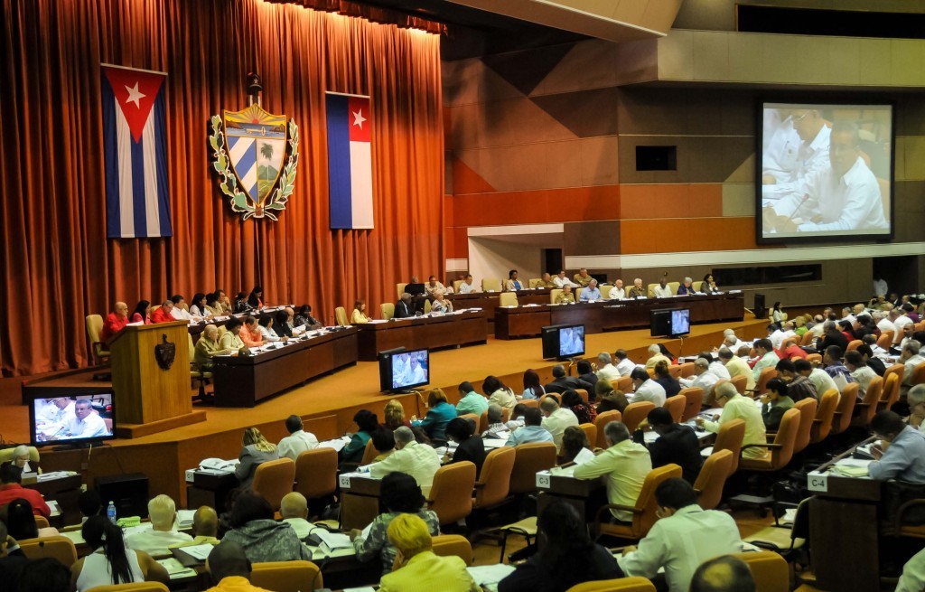 Cuban parliament with flags and coat of arms hanging in front of curtains