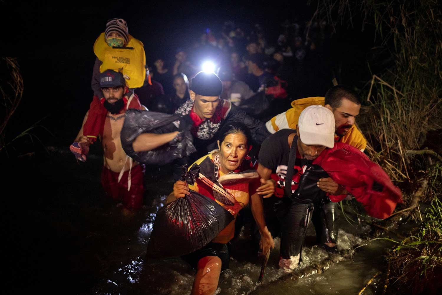 migrants crossing in the dark, one holding a lantern high