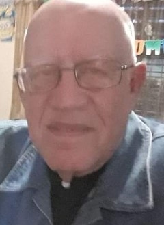 Foto de hombre de pelo blanco con lentes y camisa oscura mirando a la cámara