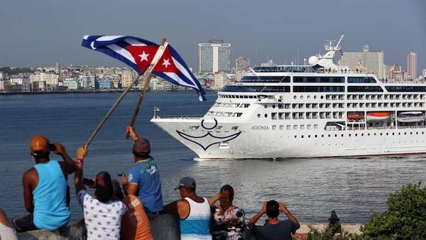 cruise ship arriving in Havana harbor with people on shore holding up Cuban flags