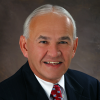white haired smiling man with suit and red tie