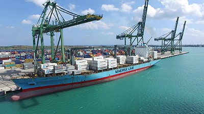 Commercial transport ship with cranes on a aqua colored bay with a blue sky and white clouds