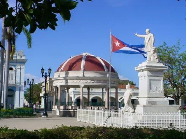 Mercedes Rodriguez Rodriguez - Parque José Martí, Cienfuegos, Cuba Estatuas en un parque con la bandera cubana y cielo azul