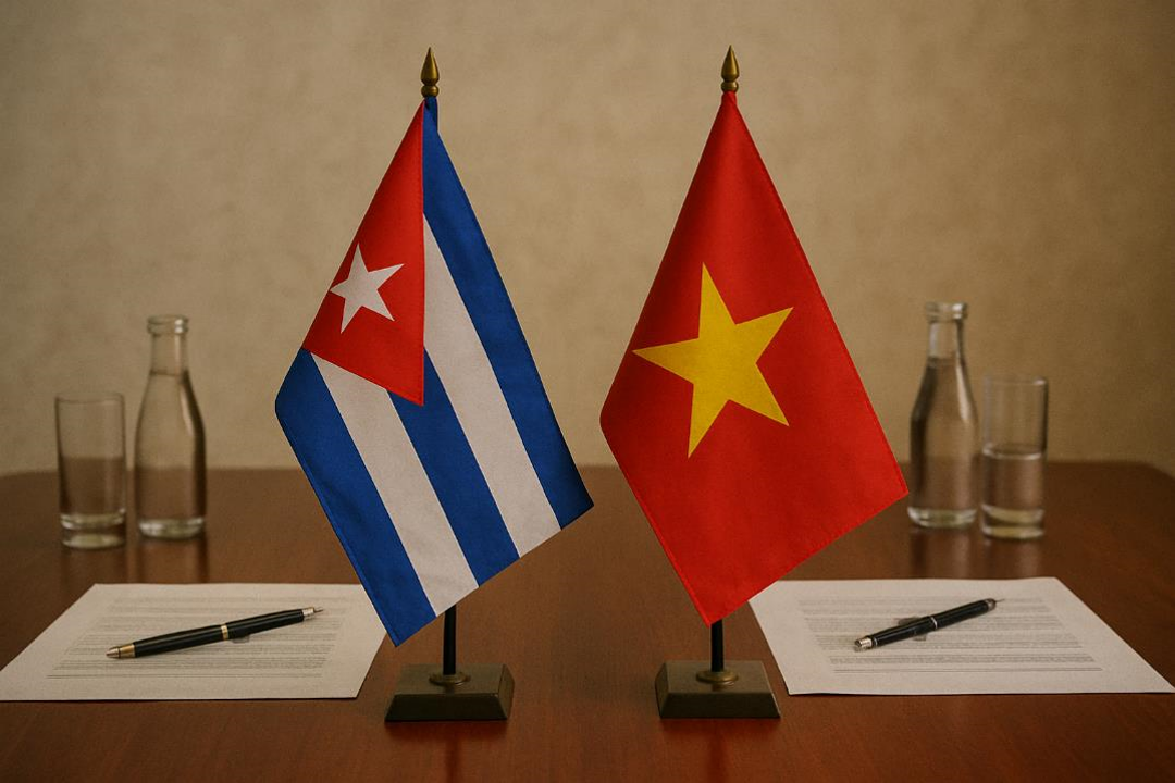 On a polished wooden table, two small flags are placed side by side. On the left is the Cuban flag, with blue and white stripes and a red triangle with a white star. On the right is the Vietnamese flag, red with a large yellow star in the center. In front of each flag is a document with a pen, and further back are bottles and glasses of water. The atmosphere conveys formality and cooperation between the two countries. 