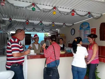 personas de espalda comiendo en un mostrador atendidas con mujer con gorra roja bajo techo con decoraciones de navidad