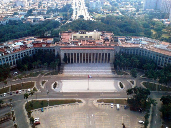 Vista aérea de la Plaza de la Revolución en La Habana, con el edificio principal de columnas al centro, el Palacio de la Revolucion, una amplia explanada y avenidas rodeadas de áreas verdes.