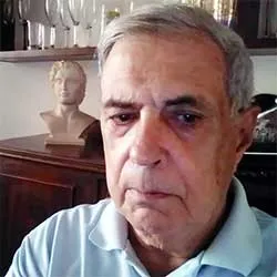hombre mirando la camara de reojo con pelo canoso y camisa azul clara