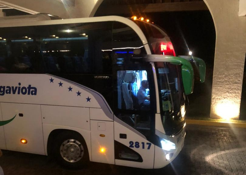 The image shows a white Gaviota tourist bus parked at night under an illuminated structure, with its lights on and the driver visible through the windshield.