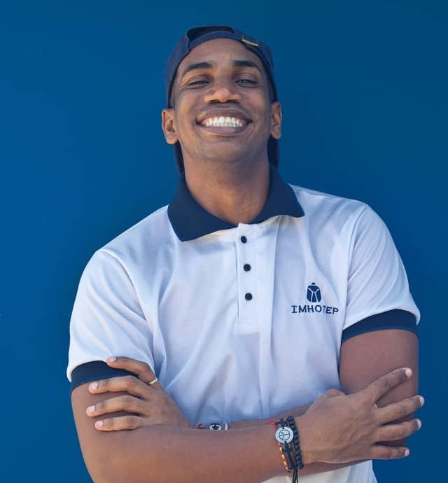 Imagen de hombre vestido de blanco sonriendo frente a un muro azul.