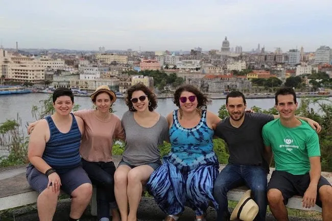 Seis jóvenes sentados en un muelle con el panorama de la bahía de La Habana en la distancia.