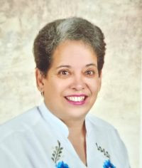 Mujer vestida de camisa blanca con detalles azul mirando a la camara y sonriendo.