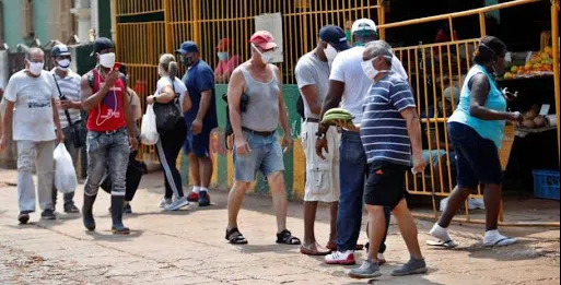 hombre saliendo de tienda con dos plátanos con una cola de gente esperando entrar