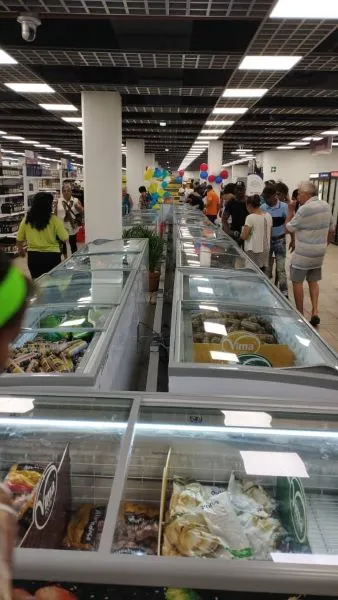 line of refrigerated glass containers filled with food with customers walking in aisles on either side