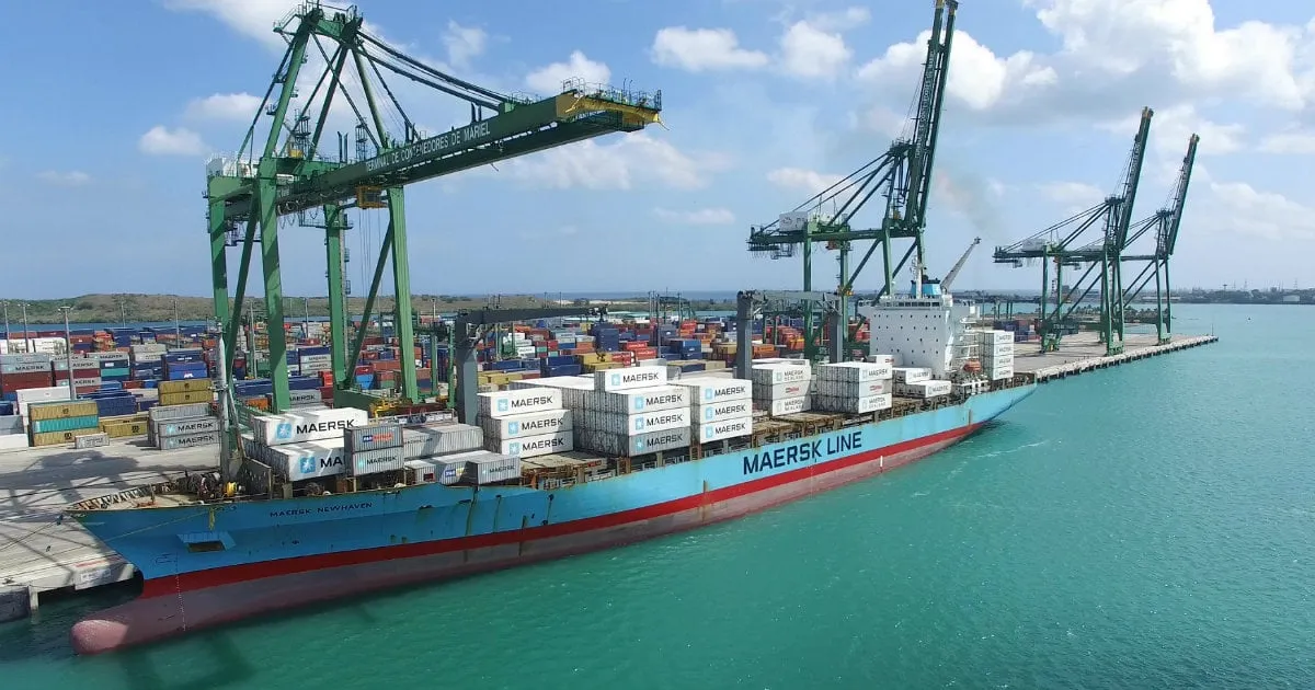 cargo ship with cranes in the background blue sky and green water