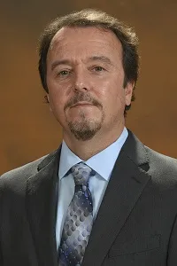 man in dark suit with blue shirt and tie looking at the camera