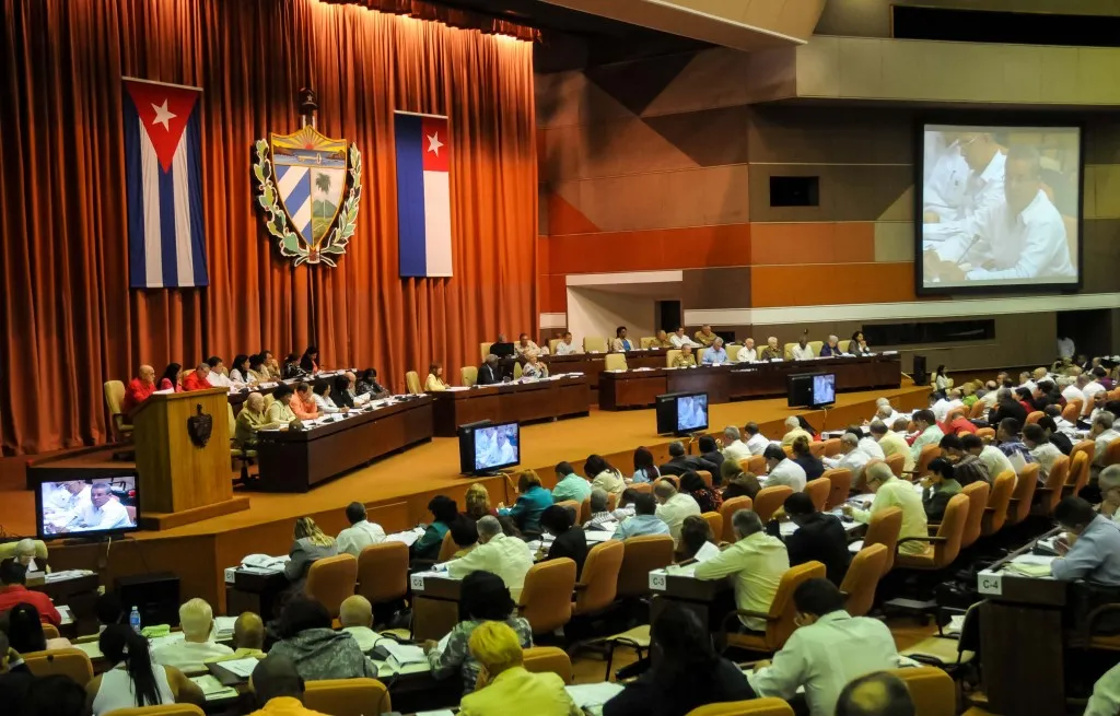 Parlamento cubano con banderas y escudos colgando frente a las cortinas