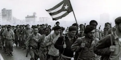 People marching along Havana’s Malecón, some carrying berets and rifles, and one carrying the Cuban flag.