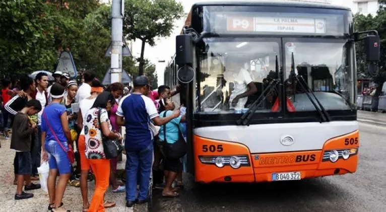 Autobus con franja roja y personas esperando en cola para montar
