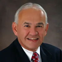 white haired smiling man with suit and red tie